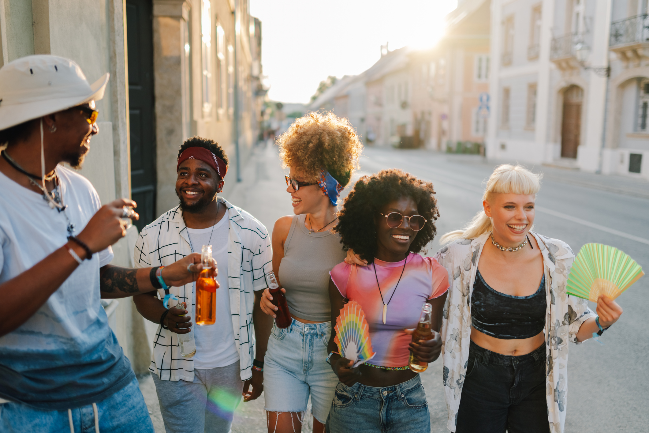 Young tourists walking down the street, drinking beer and having fun at sunset